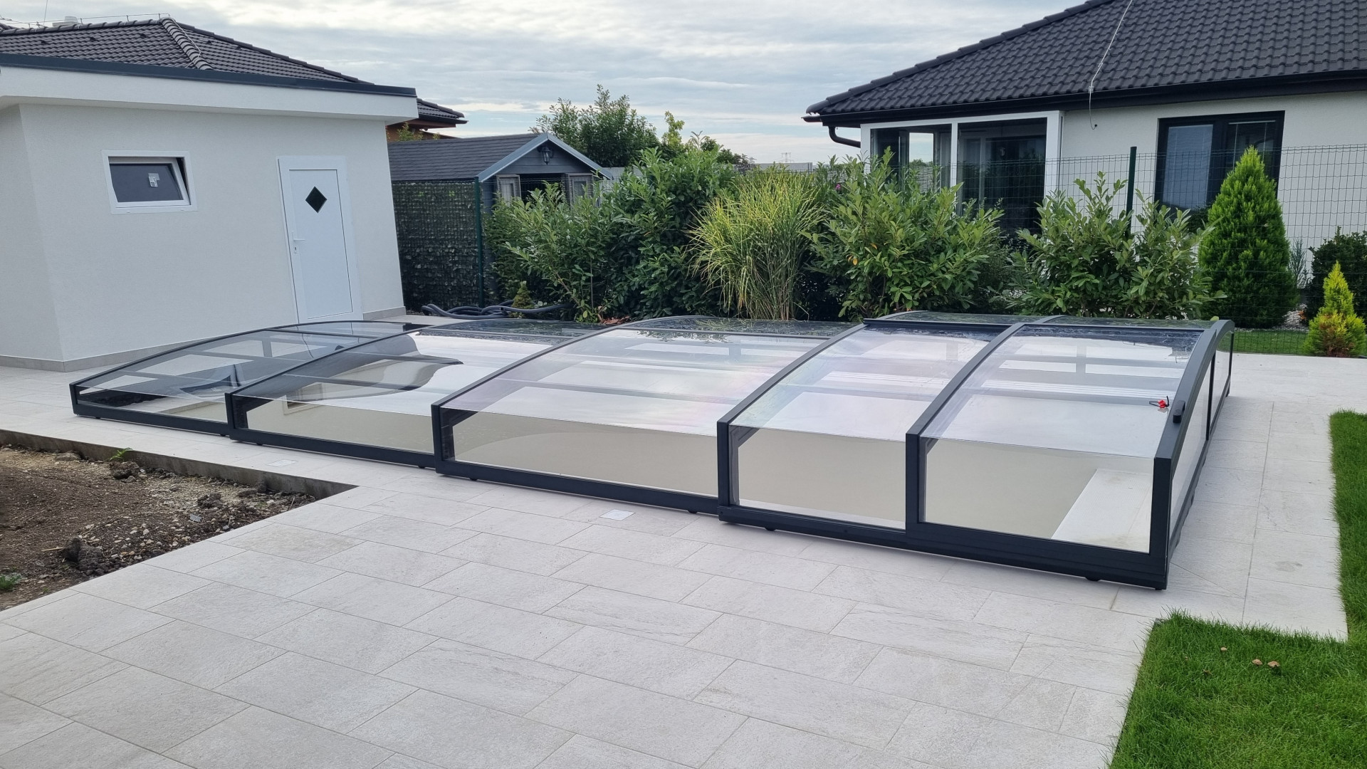 Moderne, niedrige Schwimmbadüberdachung mit schwarzem Profil auf der Terrasse eines Einfamilienhauses