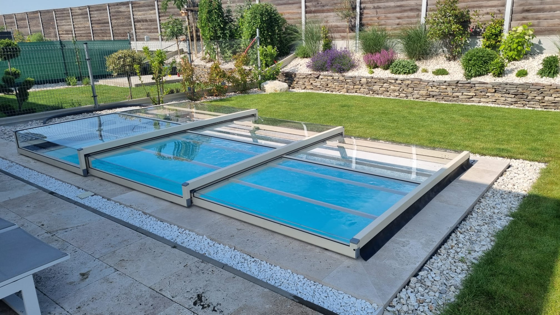 Eine moderne, niedrige Teleskop-Schwimmbadüberdachung mit verglasten Segmenten in einem gepflegten Garten.