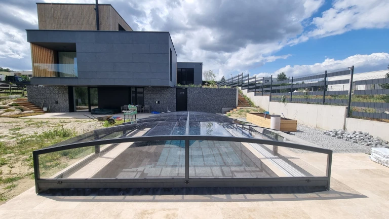 Ein modernes Einfamilienhaus mit einem niedrigen, anthrazitfarbenen Dach über dem Pool auf der Terrasse.