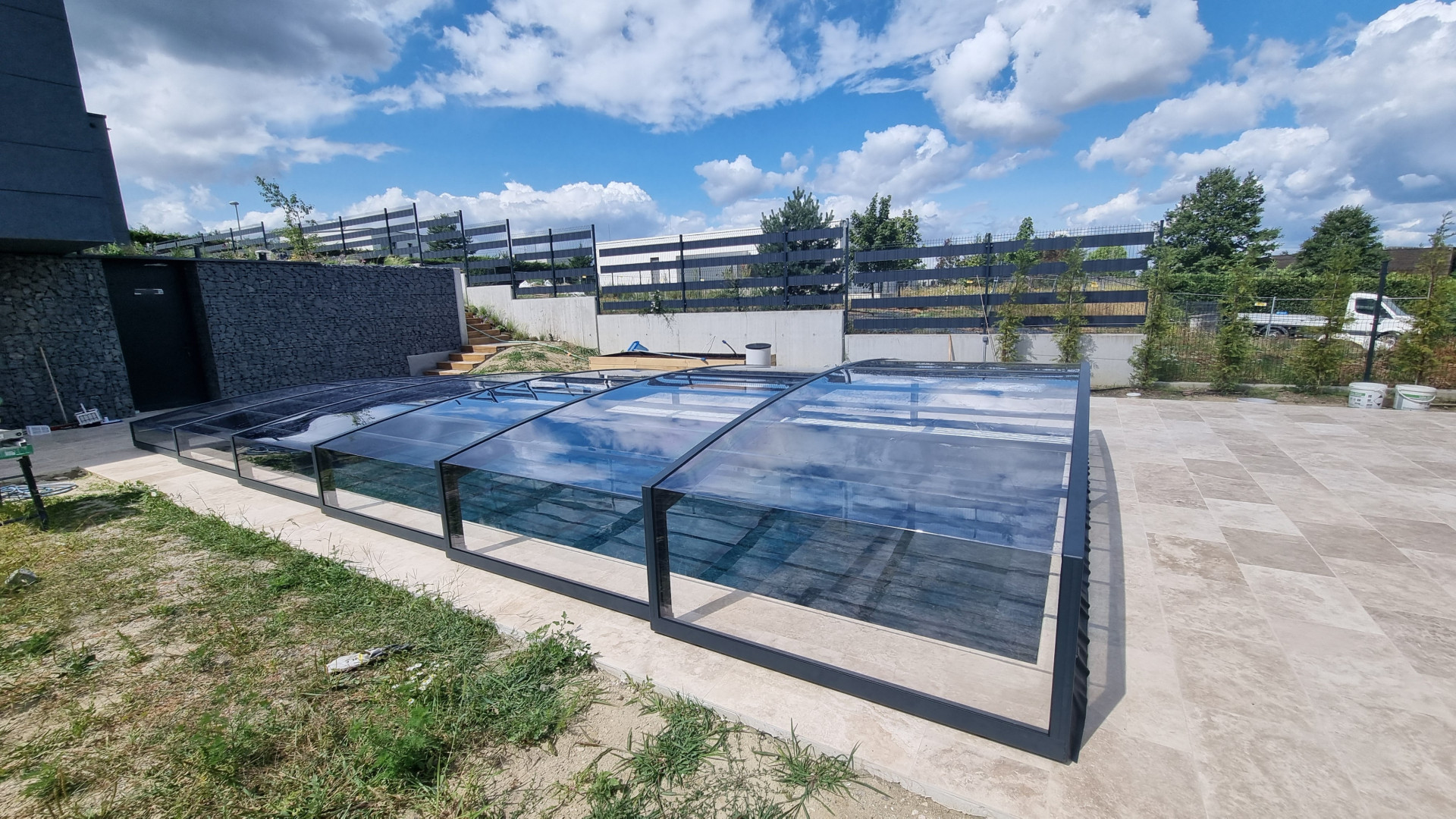 Moderne, niedrige Schwimmbadüberdachung mit dunklen Profilen und transparenter Verglasung auf der Terrasse eines Einfamilienhauses