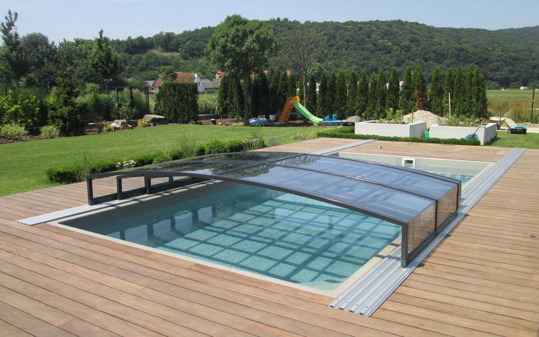 Ein modernes Schwimmbad mit einer eleganten, niedrigen Überdachung und einer Holzterrasse im Garten.