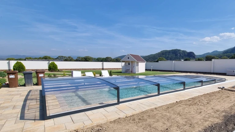Moderne, niedrige Aluminium-Schwimmbadüberdachung mit anthrazitfarbenem Rahmen und klarer Verglasung im Garten eines Einfamilienhauses