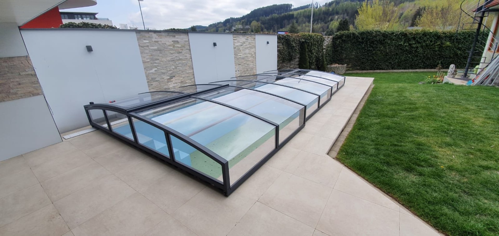 Moderne, niedrige Schwimmbadüberdachung mit anthrazitfarbenem Rahmen auf der Terrasse am Garten
