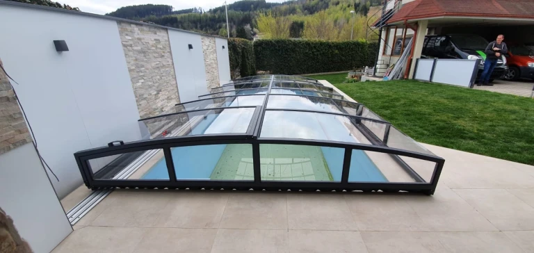Moderne, niedrige Schwimmbadüberdachung mit schwarzer Konstruktion und Glaselementen im Garten