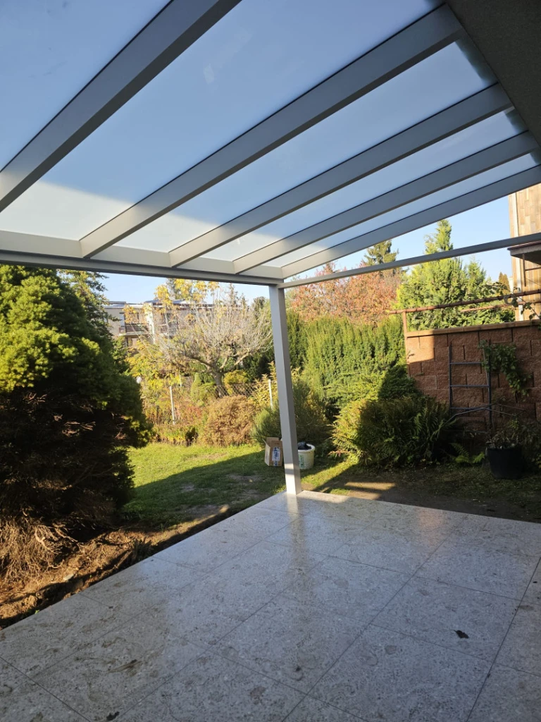 Eine moderne Aluminium-Pergola mit Glasdach über der Terrasse mit Blick auf den Garten