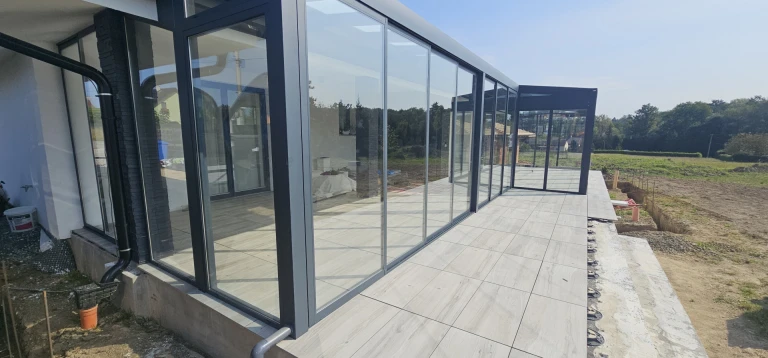 Ein moderner, verglastes Wintergarten mit einer anthrazitfarbenen Aluminiumkonstruktion und einer gepflasterten Terrasse.