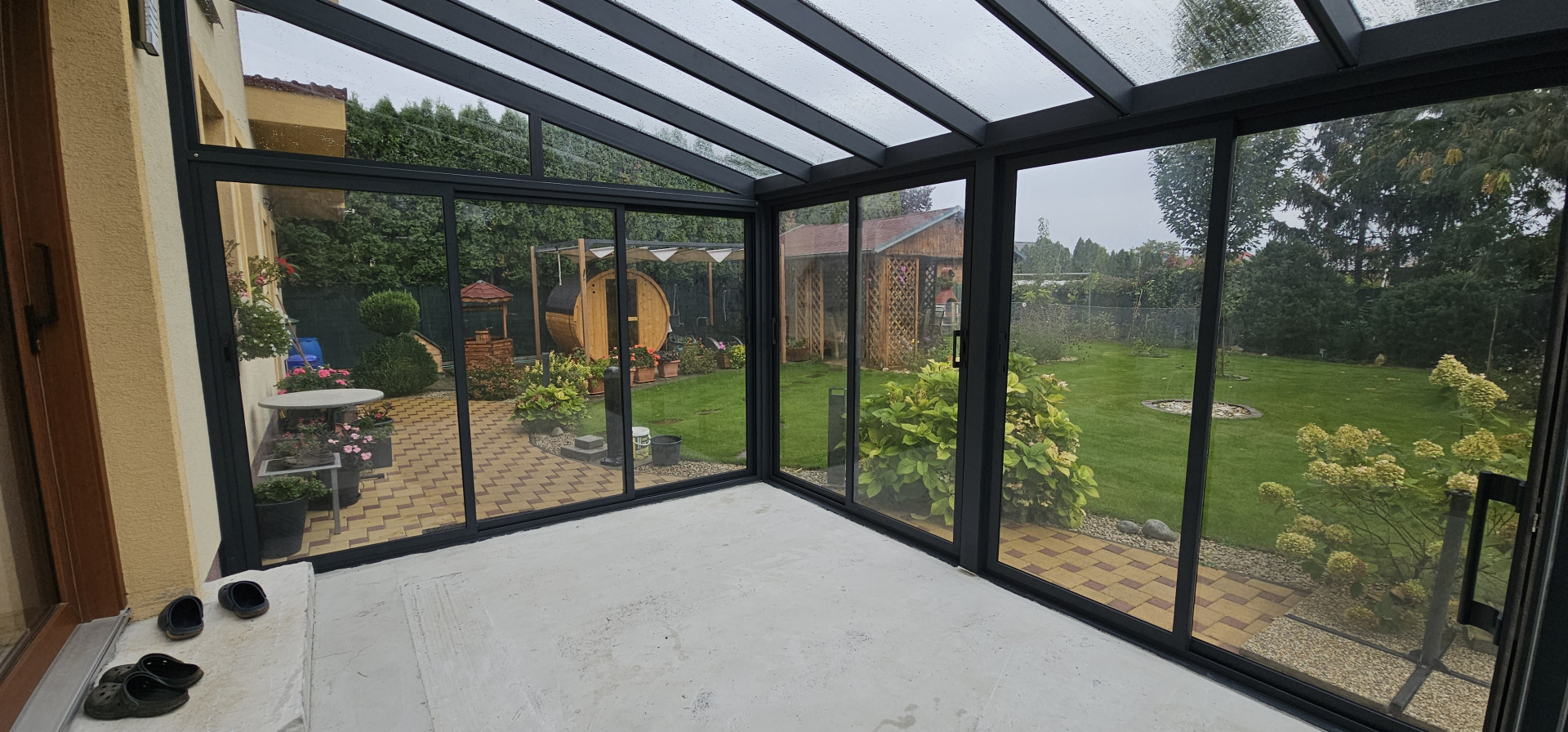 Ein moderner, verglaster Wintergarten mit schwarzem Aluminiumrahmen und Blick auf den Innenhof mit Sauna