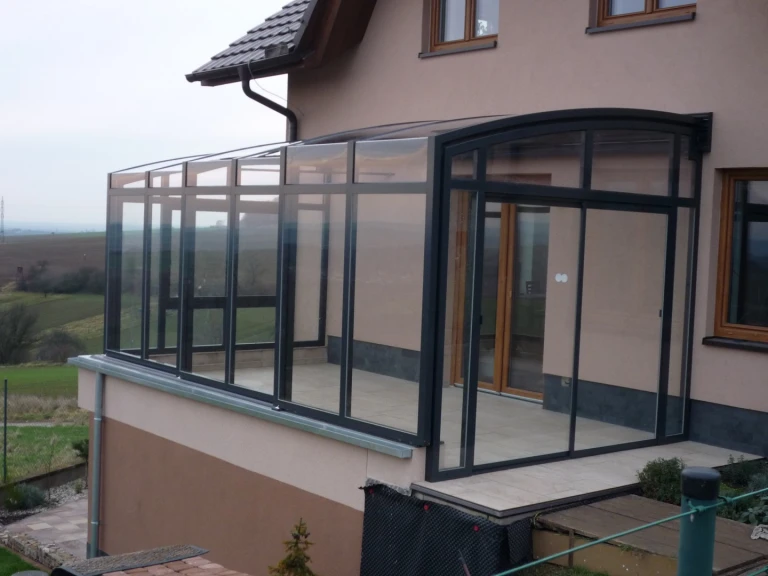 Ein moderner Wintergarten mit Schiebekonstruktion aus anthrazitfarbenem Aluminium und Verglasung auf der Terrasse eines Einfamilienhauses.