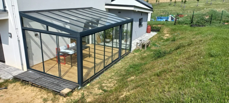 Ein moderner, verglaster Wintergarten mit anthrazitfarbener Konstruktion und Holzboden an einem Einfamilienhaus