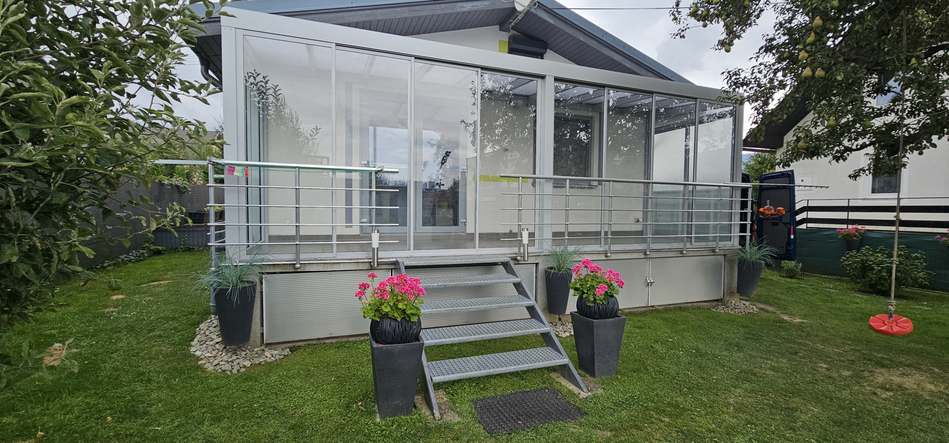 Ein moderner, verglaster Wintergarten auf einer erhöhten Terrasse mit Treppe und Blumendekoration