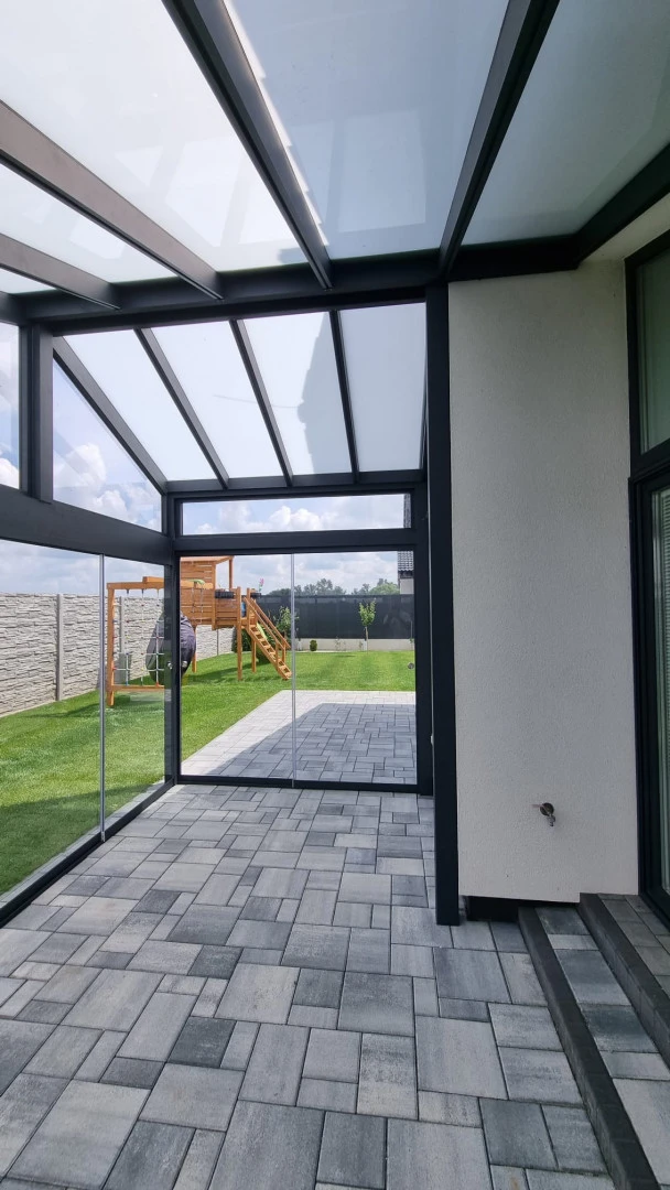 Ein verglaster Wintergarten mit Aluminiumkonstruktion und Blick auf den Hof mit Kinderspielplatz