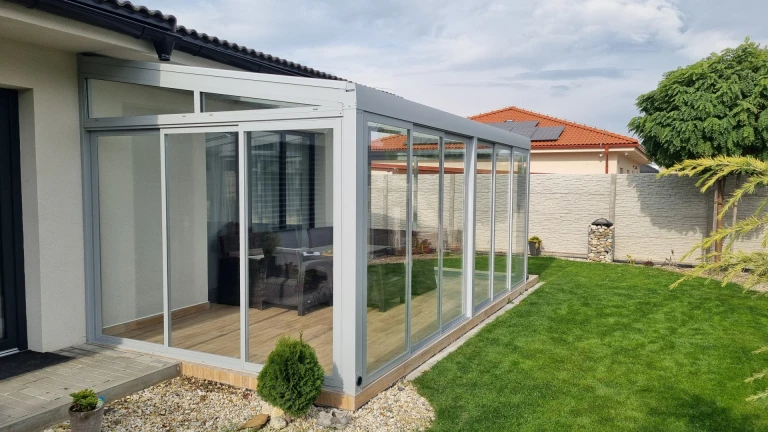 Ein moderner, verglaster Wintergarten mit Aluminiumkonstruktion, der an ein Einfamilienhaus mit Garten angebaut ist