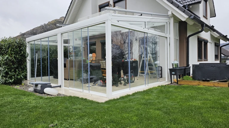 Ein moderner, verglaster, weißer Wintergarten aus Aluminium an einem Einfamilienhaus mit Garten