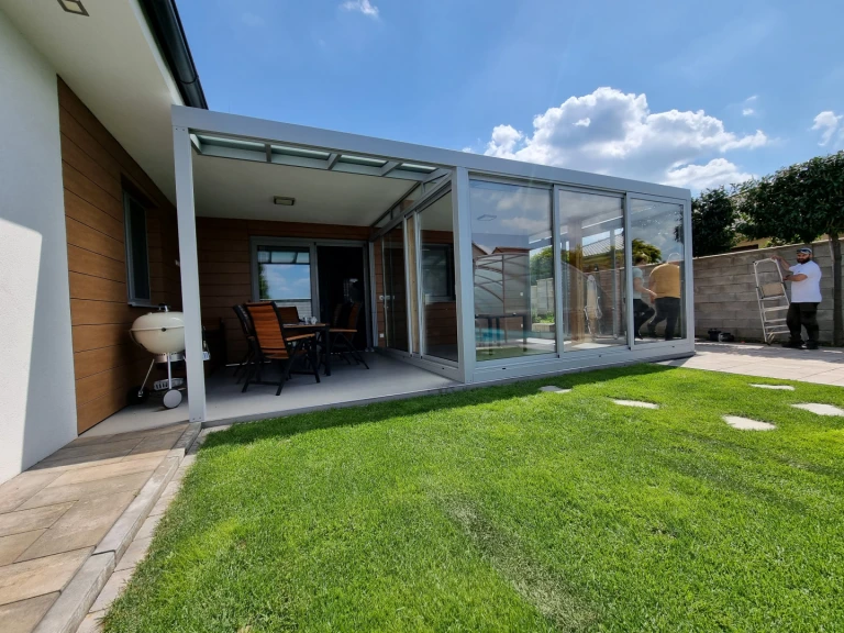 Ein moderner, verglastes Wintergarten mit Aluminiumkonstruktion, der an ein Einfamilienhaus mit gepflegtem Rasen angebaut wurde.