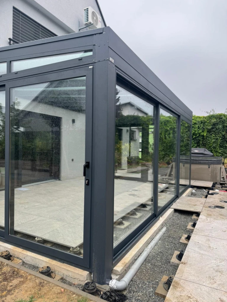 Moderne, verglaste Wintergartenkonstruktion mit dunkelgrauem Aluminiumrahmen in der Bauphase an einem Einfamilienhaus.