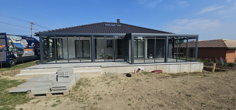 Ein moderner, verglaster Wintergarten mit anthrazitfarbener Konstruktion, der an ein Einfamilienhaus angebaut ist