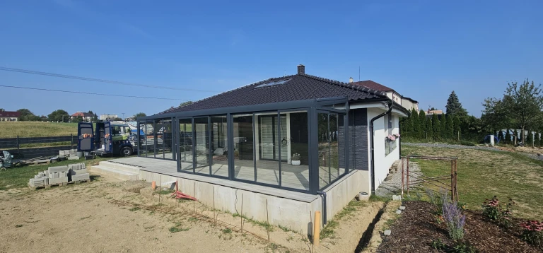 Ein moderner, verglaster Wintergarten mit anthrazitfarbener Konstruktion, der an ein Einfamilienhaus angebaut wurde
