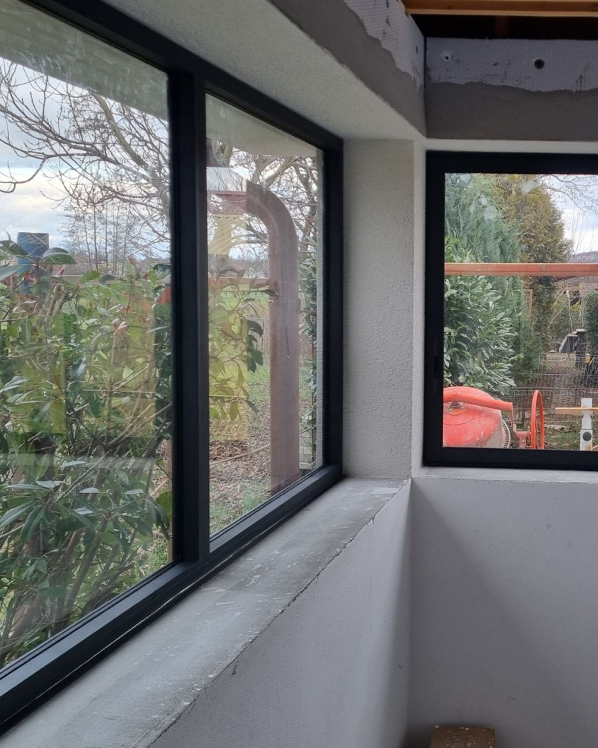 Ein Detailblick auf die Eckverglasung der Terrasse mit dunklen Aluminiumrahmen und Blick in den Garten.