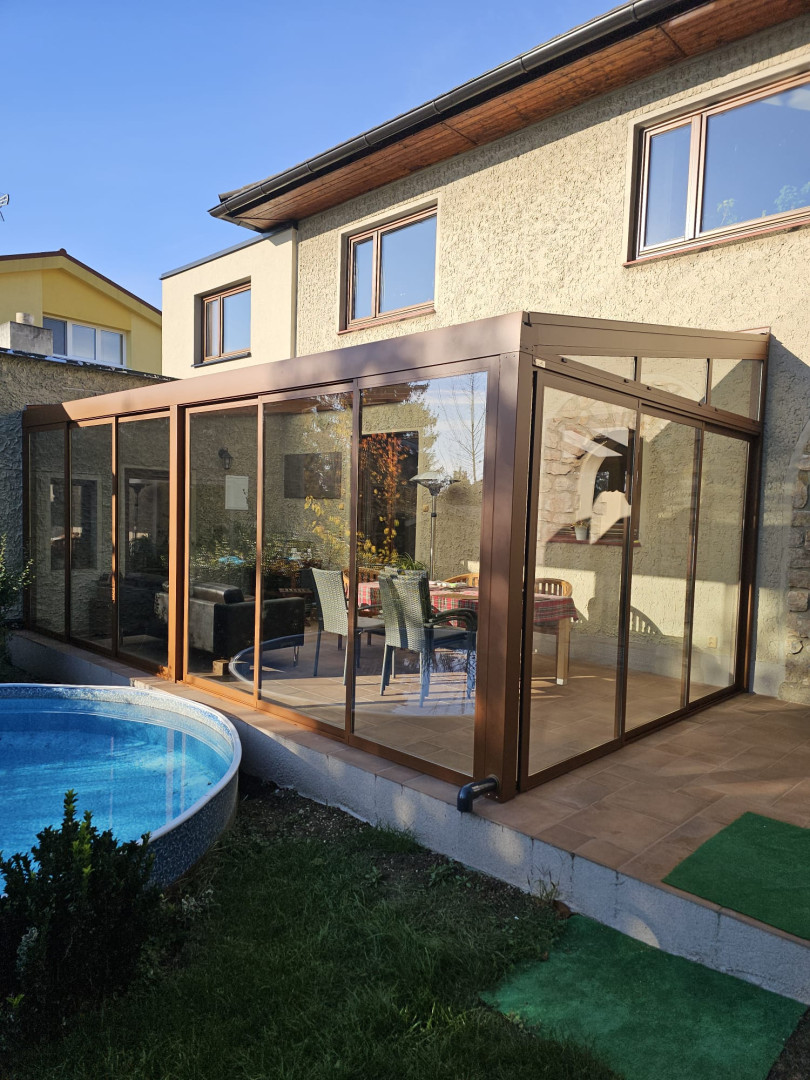 Ein moderner, verglaster Wintergarten mit brauner Konstruktion an einem Einfamilienhaus mit Swimmingpool