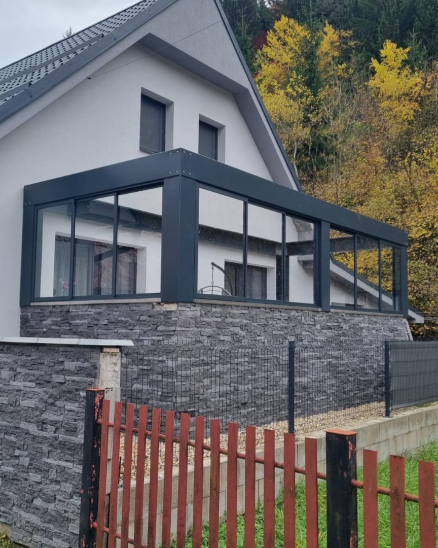 Moderne Terrassenverglasung an einem Einfamilienhaus mit dunklem Rahmen und Steinverkleidung