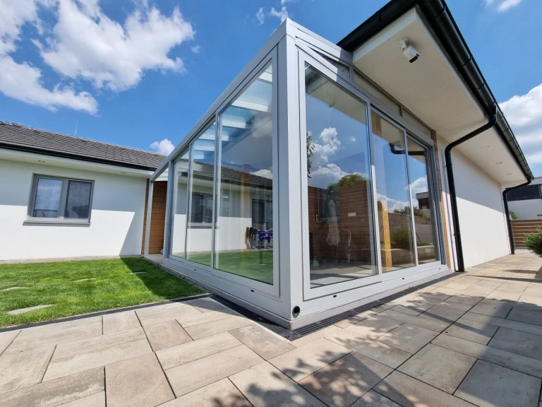 Ein moderner, verglaster Wintergarten mit Aluminiumkonstruktion, der an ein Einfamilienhaus angebaut ist und einen Blick auf den Rasen bietet