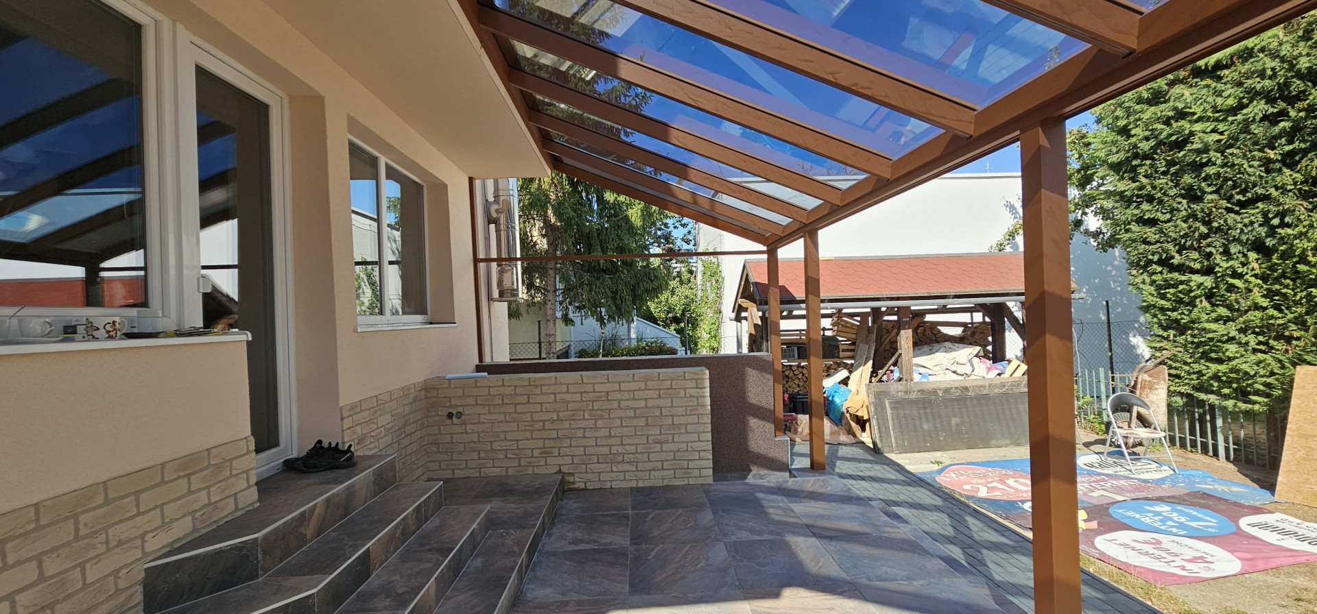 Eine Aluminium-Pergola in Holzoptik mit Glasdach, die auf der Terrasse eines Einfamilienhauses montiert wurde.