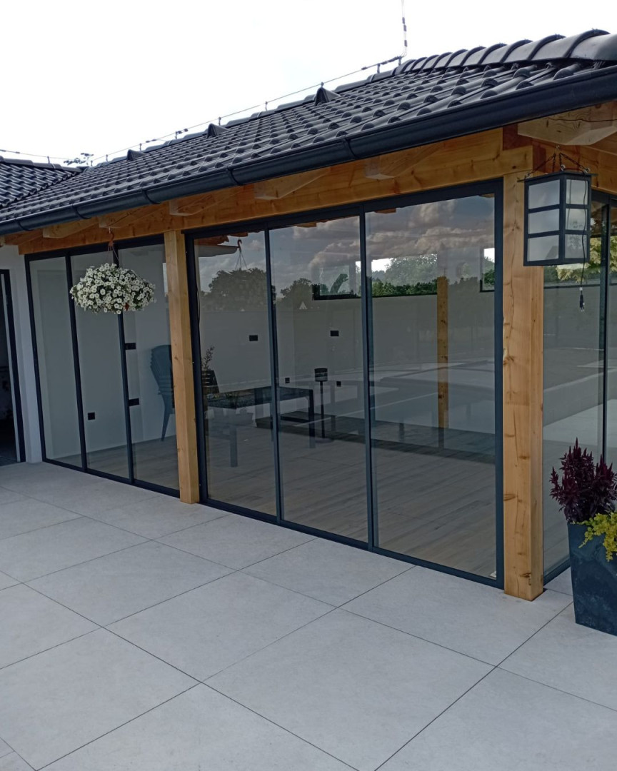 Moderne Terrassenverglasung mit Schiebesystem in Holzbauweise unter einem dunklen Dach.
