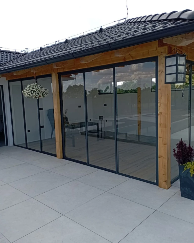 Moderne Terrassenverglasung mit Schiebesystem in Holzbauweise unter einem dunklen Dach.
