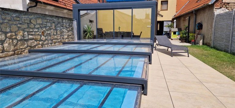Moderne, niedrige Teleskop-Schwimmbadüberdachung mit anthrazitfarbenem Aluminiumrahmen auf der Terrasse neben dem Haus.