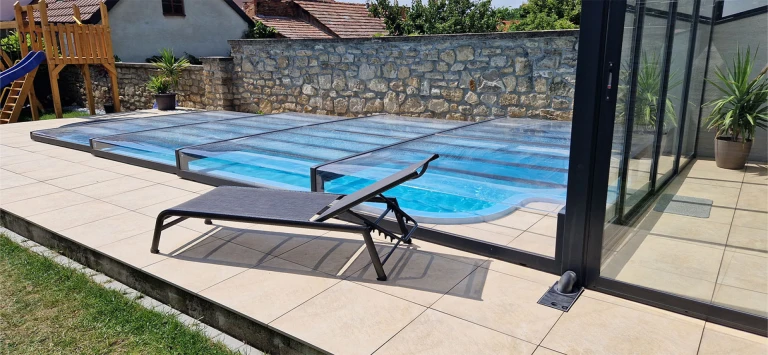 Moderne, niedrige Schwimmbadüberdachung mit schwarzem Aluminiumrahmen auf der Terrasse mit Liegestuhl