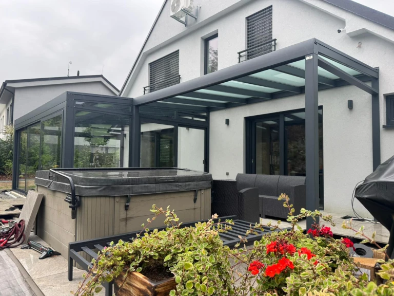 Ein moderner, verglaster Anbau an ein Einfamilienhaus mit Terrasse, Whirlpool und Gartenmöbeln.