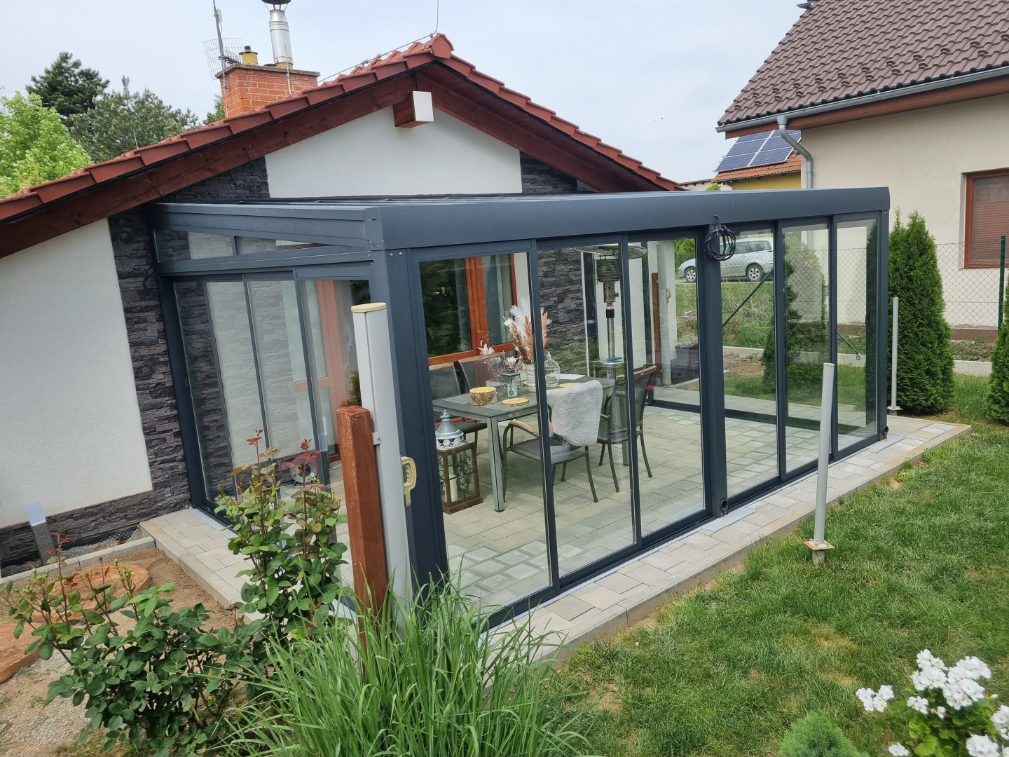 Ein moderner, verglaster Wintergarten mit anthrazitfarbener Konstruktion und Schiebetüren an einem Einfamilienhaus