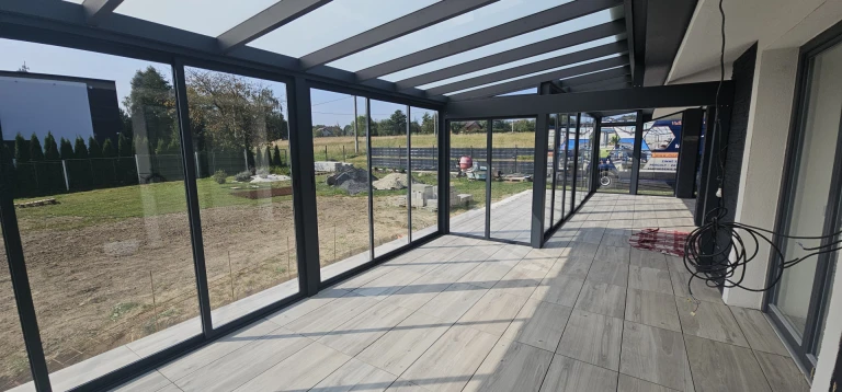 Ein moderner, verglaster Wintergarten mit anthrazitfarbener Konstruktion und Blick ins Freie