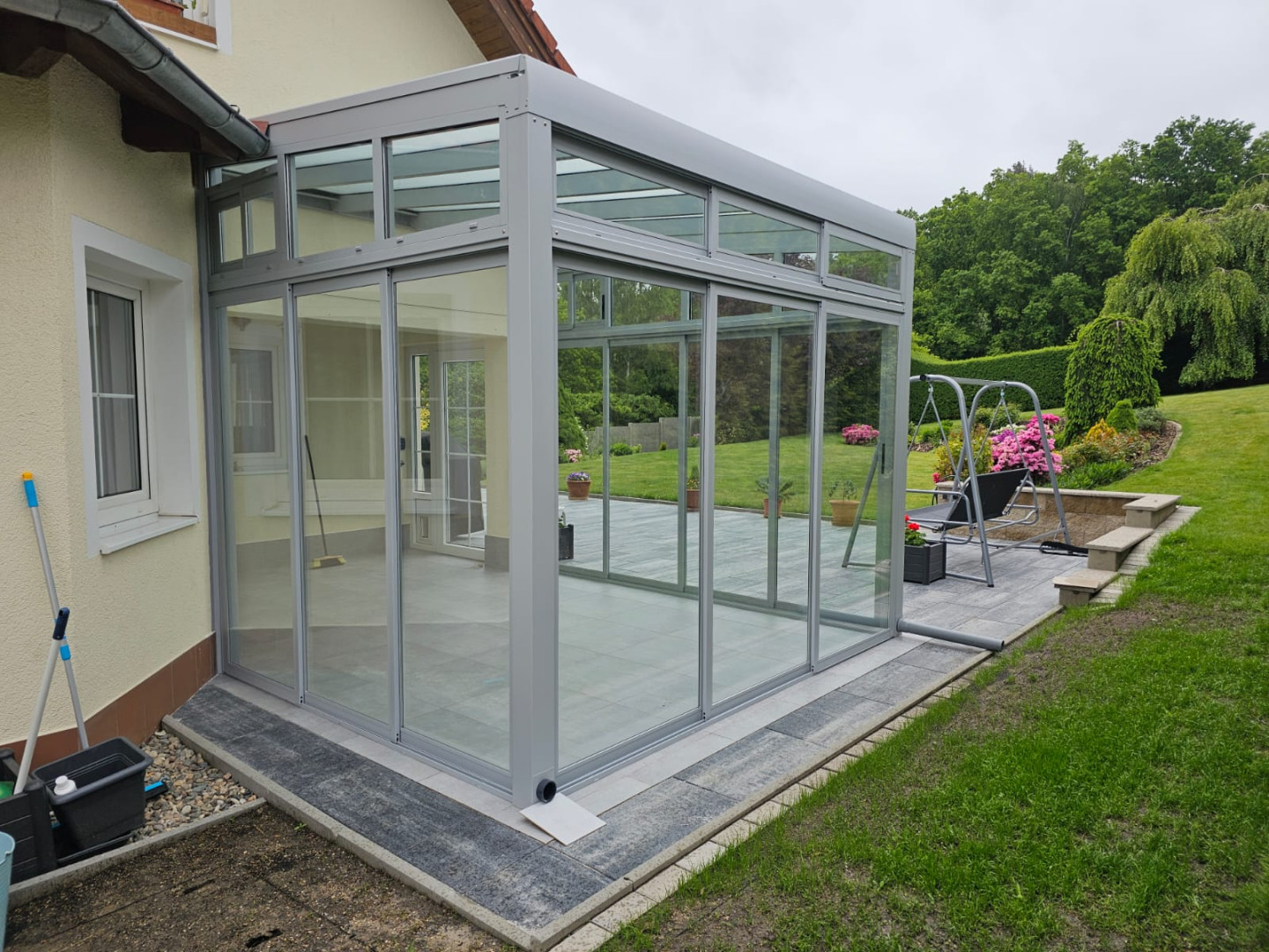Ein moderner, verglaster Wintergarten mit Aluminiumkonstruktion, der an ein Einfamilienhaus angebaut ist