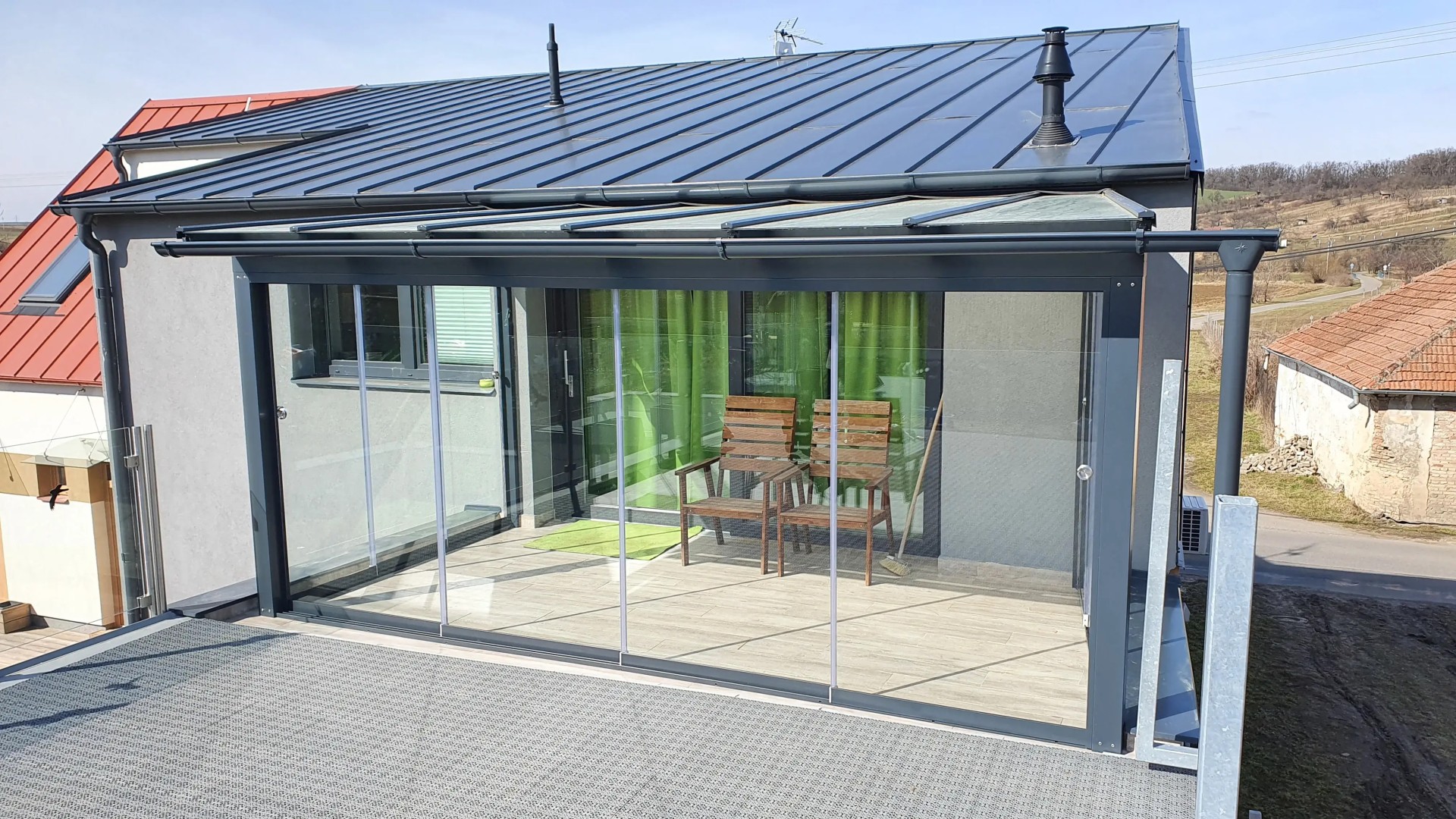 Ein moderner, verglaster Wintergarten mit anthrazitfarbener Konstruktion und Schiebefenstern auf der Terrasse des Hauses.