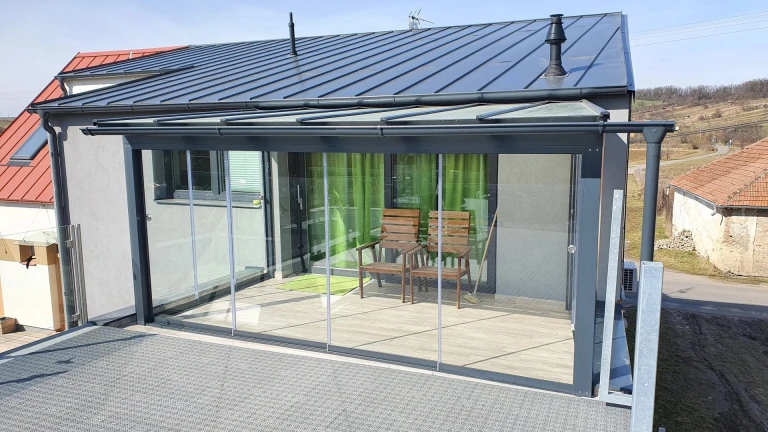 Ein moderner, verglaster Wintergarten mit anthrazitfarbener Konstruktion und Schiebefenstern auf der Terrasse des Hauses.